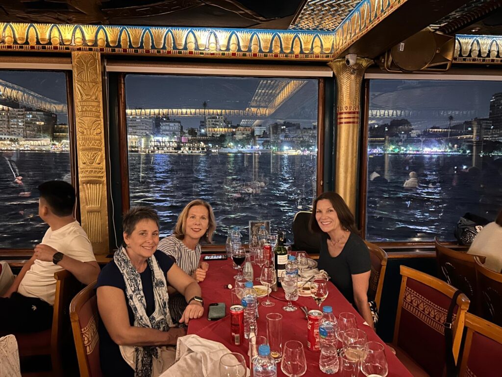 Three women smiling are out to eat at night on a Nile River cruise in Egypt.