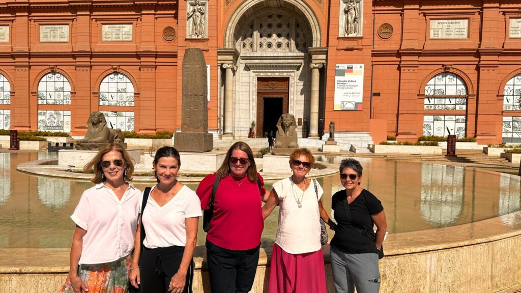 A group of five women pose for a picture in front of a large, cultural building in Egypt.