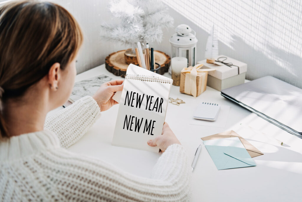 Woman sitting at a desk looks at a notebook where she has written "New year new me" in black ink.