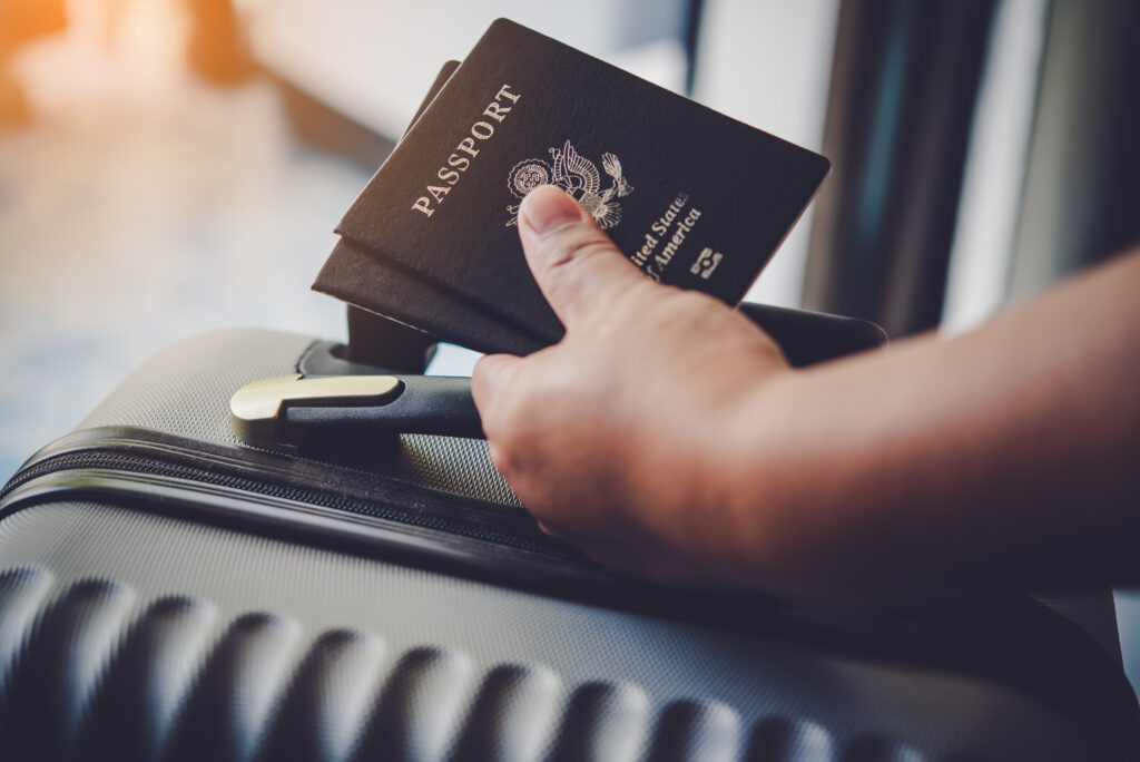 A hand resting on a suitcase while holding two passports.