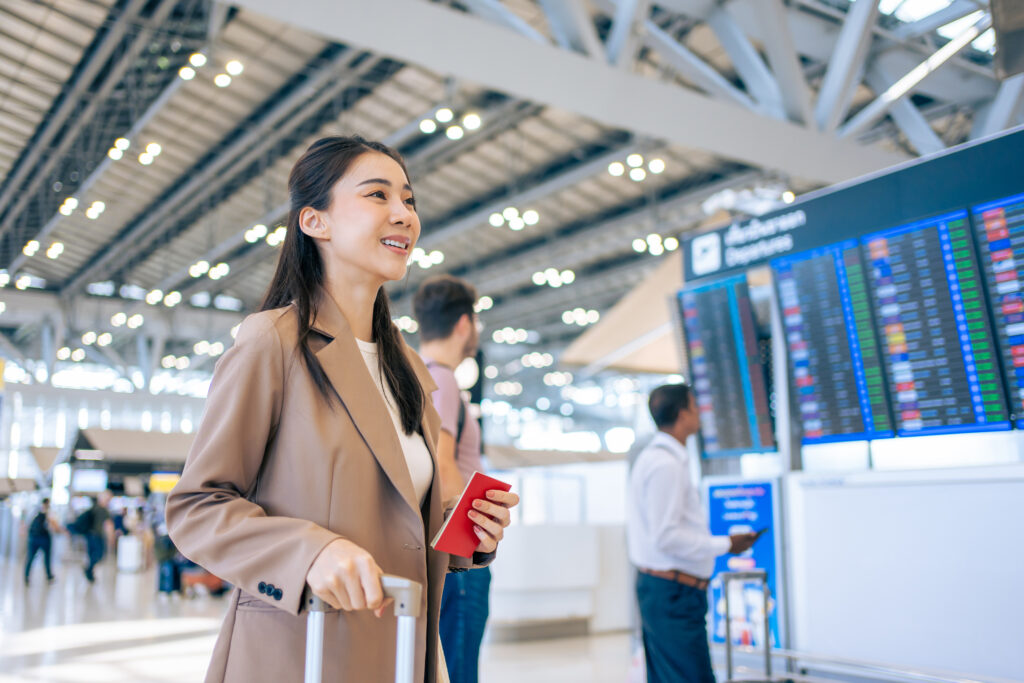 A young smiling Asian woman walks through an airport with her passport.